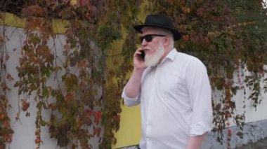 Albinizmli yaşlı adam evinin yanında yürürken telefonla konuşuyor..