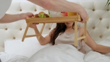 Kadın yatakta uzanıp kitap okurken kocası kahvaltıyla geliyor..