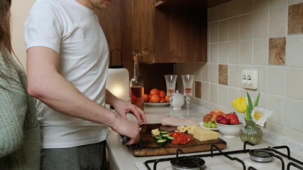 Ung kvinna ger gåva till sin man som lagar mat i köket. — Stockvideo