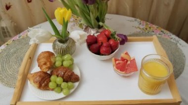Odun tepsisini portakal suyu, meyve kruvasanı ve çiçeklerle kapat ve bardağı üzerine koy..