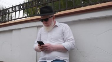 Evinin yanında otururken internette gezinen albinizm hastası yaşlı bir adam..