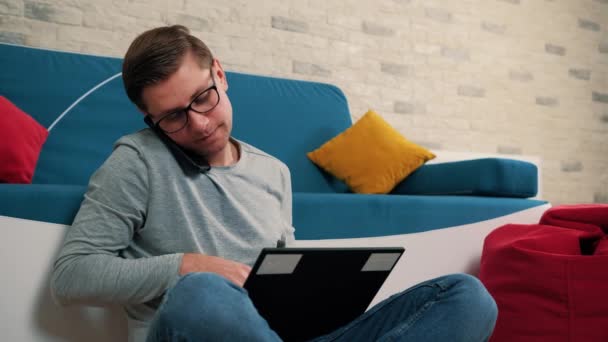 Young mantalking aan de telefoon tijdens het schrijven van een bericht op laptop, geïsoleerd thuis. — Stockvideo