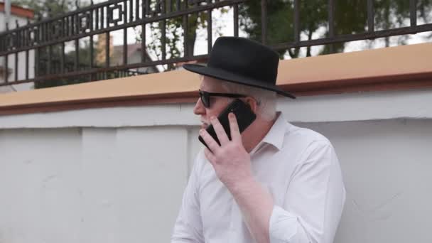 Velho com albinismo falando ao telefone enquanto sentado ao lado de sua casa. — Vídeo de Stock