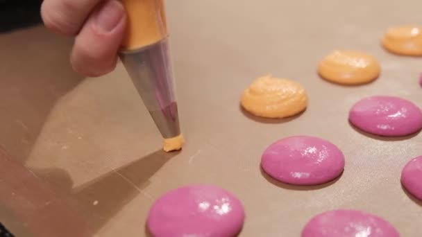 Chef-kok van een roze en oranje macarons, giet de vulling op het bakpapier. — Stockvideo