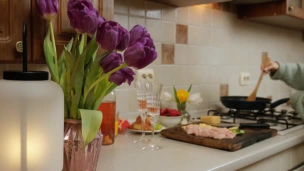 Vlakbij de keukentafel met bloemen, wijn en eten, bereidt de vrouw het diner. — Stockvideo