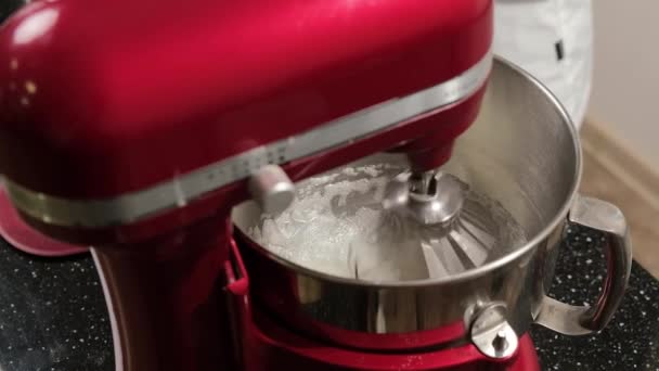 Red mixer which is whipping the egg whites in a stainless bowl in the kitchen. — Stok video