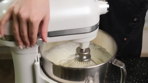 Valkoinen mikseri, joka on kermavaahtoa ruostumattomassa kulhossa keittiössä. — kuvapankkivideo