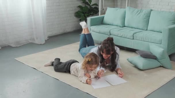 Mamma och dotter ligger på mattan på golvet och ritar på papper tillsammans.. — Stockvideo