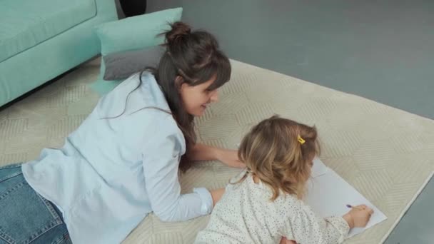 Mutter und Tochter liegen auf Teppich auf dem Boden und zeichnen gemeinsam auf Papier. — Stockvideo