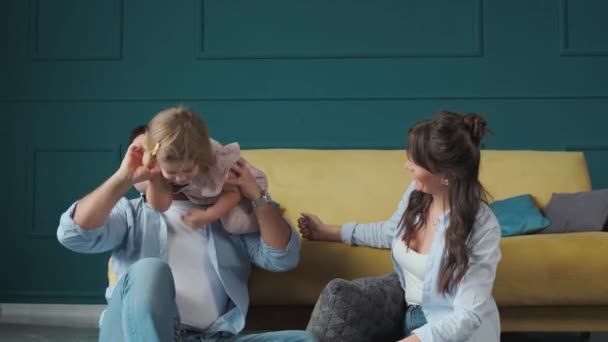 Jovens pais felizes estão sorrindo, abraçando e brincando com sua filhinha. — Vídeo de Stock