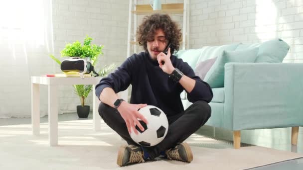 Homem de pé com bola de futebol nas mãos e falando ao telefone. — Vídeo de Stock