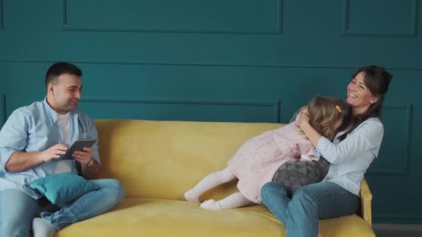 Liten flicka leker med mamma med kuddar, medan hennes far arbetar med en tablett. — Stockvideo