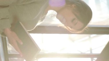 Güzel bir kadın pencerenin kenarında oturuyor ve günbatımının arka planında kitap okuyor..