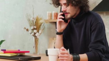 Mutfaktaki adam gülümsüyor, kahve içiyor ve akıllı bir telefonla konuşuyor..