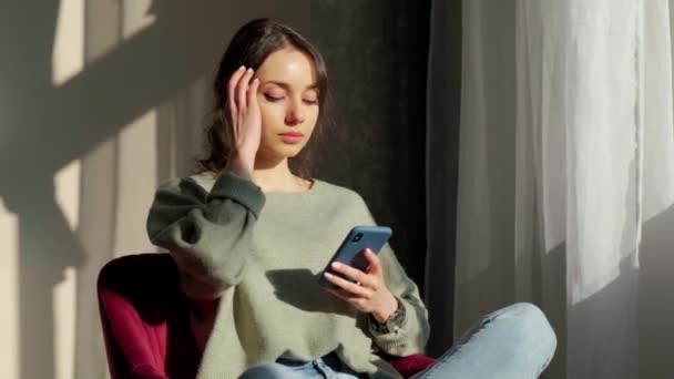 Belle femme assise près de la fenêtre et utilisant un téléphone mobile au coucher du soleil. — Video