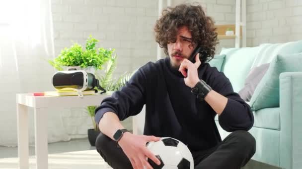 Чоловік стоїть з футбольним м'ячем в руках і розмовляє по телефону . — стокове відео