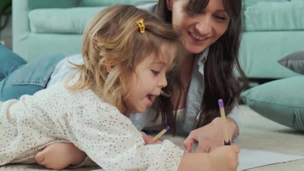 Mamá e hija tumbadas en la alfombra en el suelo, dibujando sobre papel juntas. — Vídeo de stock