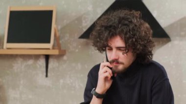 Mutfaktaki adam gülümsüyor, kahve içiyor ve akıllı bir telefonla konuşuyor..