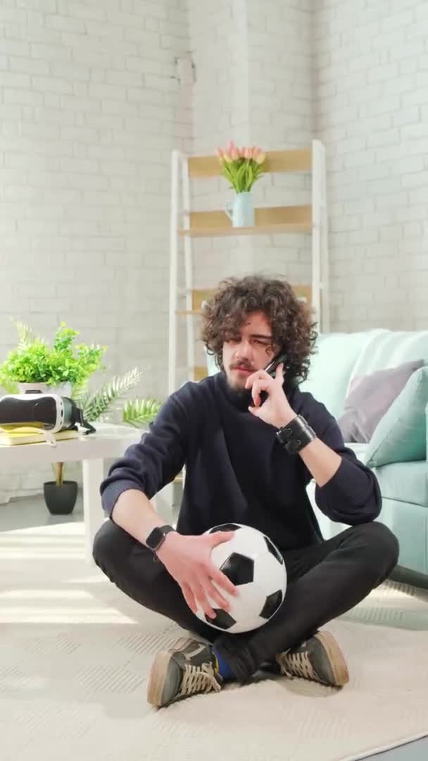 Человек, стоящий с футбольным мячом в руках и разговаривающий по телефону. — стоковое видео
