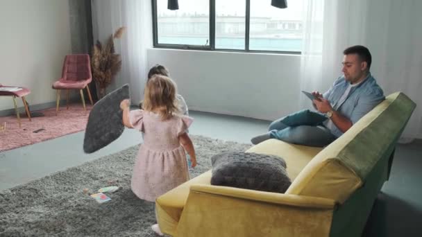 Liten flicka leker med mamma med kuddar, medan hennes far arbetar med en tablett. — Stockvideo