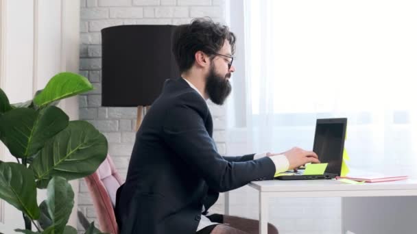 Baard man comfortabel aan zijn bureau, in ondergoed en jas werken op afstand. — Stockvideo