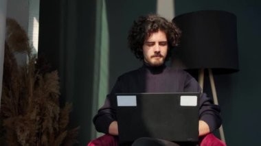 Pencerenin yanında oturan ve gün batımında dizüstü bilgisayarın başında çalışan bir adam manzaraya hayran..