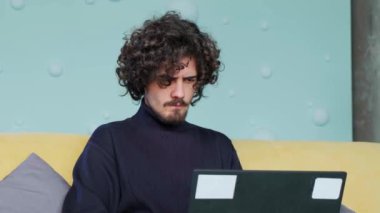 Genç adam dizüstü bilgisayarına bakıyor ve not defterine not yazıyor..