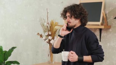 Mutfaktaki adam gülümsüyor, kahve içiyor ve akıllı bir telefonla konuşuyor..