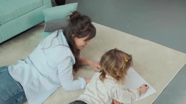 Mamma och dotter ligger på mattan på golvet, ritar på papper tillsammans. — Stockvideo