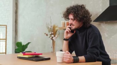 Mutfaktaki adam gülümsüyor, kahve içiyor ve akıllı bir telefonla konuşuyor..