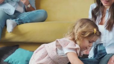 Babası tablet kullanarak çalışırken küçük kız halıda annesiyle oynuyor..
