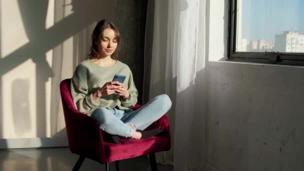 Belle femme assise près de la fenêtre et utilisant un téléphone mobile au lever du soleil. — Video