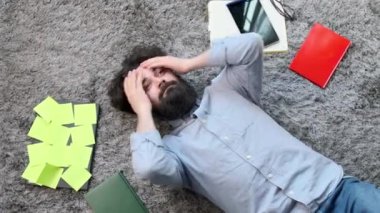 Etrafı bilgisayar ve belgelerle çevrili genç adam, çok yorgun ve yorgun..
