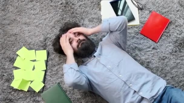 Ung man omgiven av dator och dokument, mycket trött och utmattad. — Stockvideo