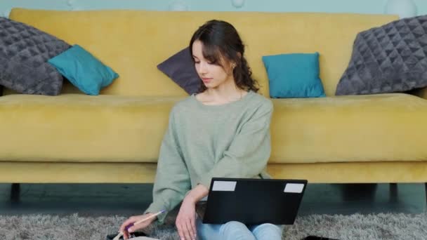 Genç kız dizüstü bilgisayarına bakıyor ve not defterine not yazıyor.. — Stok video