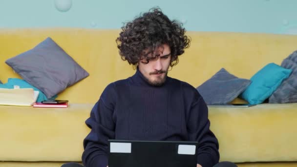 A fiatalember a laptopját nézegeti és kinyújtja a kezét, a laptopnál dolgozik.. — Stock videók