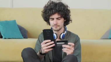 Genç adam evde akıllı telefon kullanarak internet üzerinden alışveriş yapıyor..