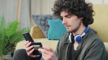 Genç adam evde akıllı telefon kullanarak internet üzerinden alışveriş yapıyor..