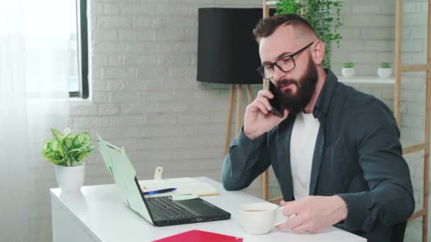 Snygg skäggig man dricker kaffe medan du pratar i en smart telefon. — Stockvideo