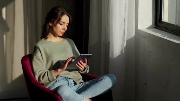 Belle femme assise près de la fenêtre et utilisant sa tablette au lever du soleil. — Video
