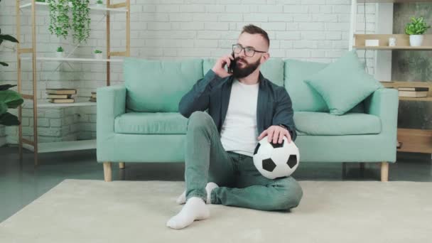 Homme debout avec ballon de football dans les mains et parlant au téléphone. — Video