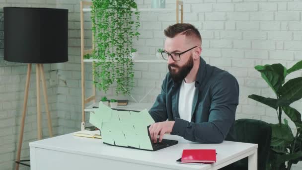 Szakállas férfi típus a laptop és írjon értesítést a papír notebook. — Stock videók