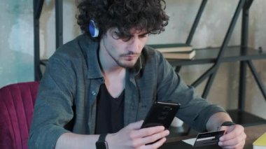 Genç adam evde akıllı telefon kullanarak internet üzerinden alışveriş yapıyor..