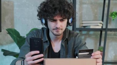 Genç adam evde akıllı telefon kullanarak internet üzerinden alışveriş yapıyor..