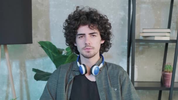 Handsome young curly haired guy looking at the camera and trying to explain something — Vídeo de Stock