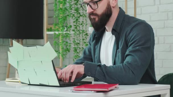 Tipos de homem barbudo no laptop e escrever aviso no caderno de papel. — Vídeo de Stock