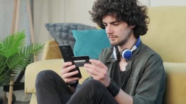 Kıvırcık saçlı adam evde akıllı telefon kullanarak online alışveriş yapıyor..