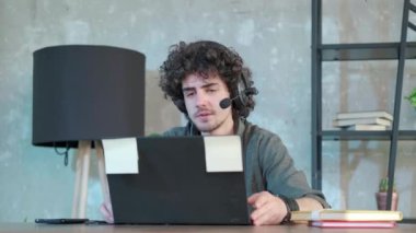 Genç kıvırcık saçlı adam internette konuşmak için dizüstü bilgisayar kullanıyor..