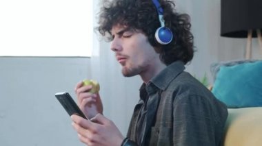 Genç adam elma yerken müzik dinleyip el kol hareketi yapıyor..