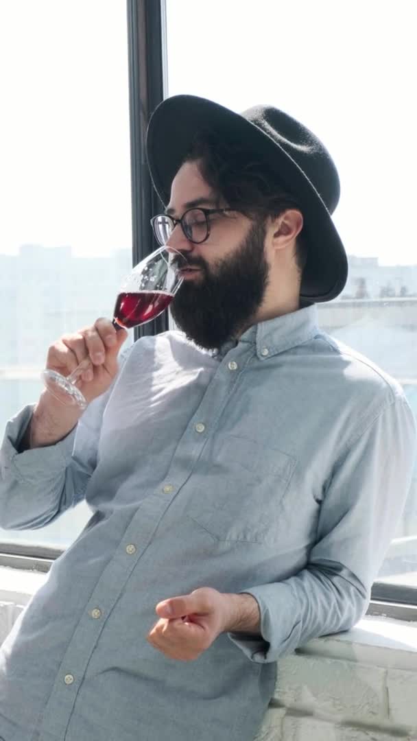 Vidám szakállas férfi iszik vörösbort és megcsodálta forma ablak otthon. — Stock videók